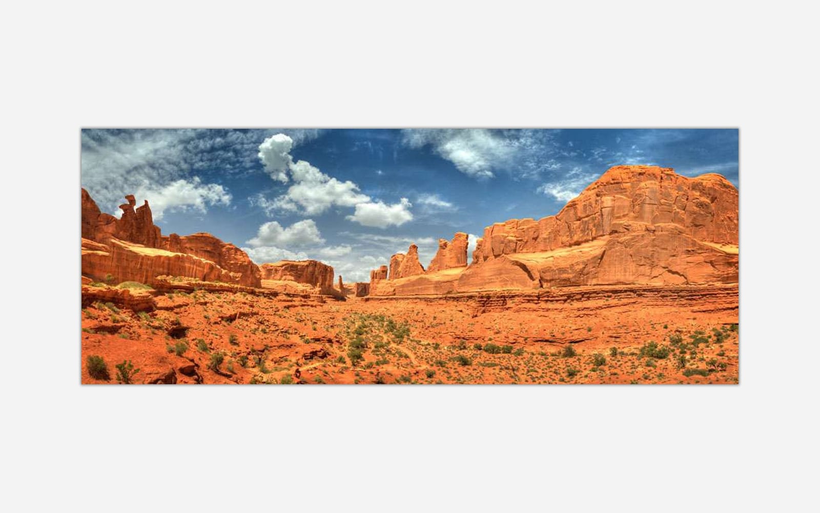 Arches A panoramic image of a desert landscape featuring red rock formations under a blue sky with clouds at Arches National Park.