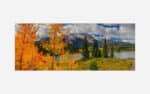 A panoramic autumn landscape with vibrant orange and yellow foliage, a serene lake, pine trees, and a mountain background under a cloudy sky.