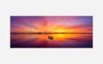A panoramic photograph of a lone boat on a still lake with a vibrant and colorful sunset reflecting on the water.