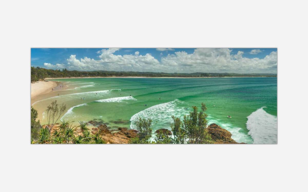 A panoramic artwork depicting a vibrant beach scene with turquoise waters, white sandy beach, waves, and green coastal vegetation.