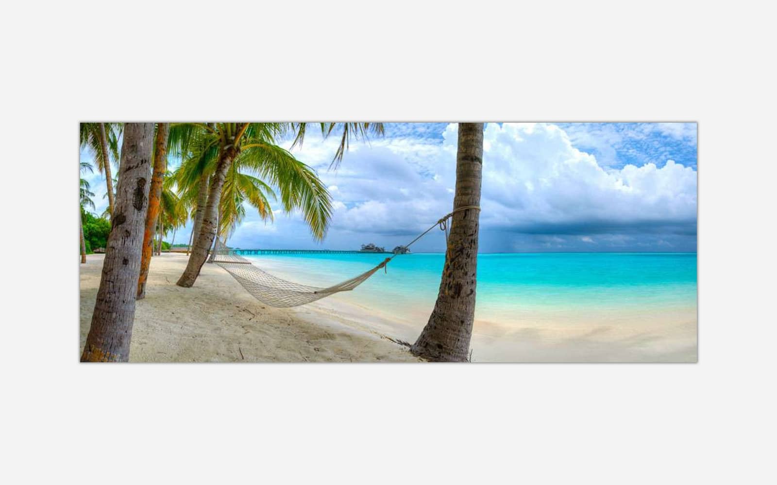 Easy Living (1) A panoramic artwork of a tranquil beach scene with a hammock tied between two palm trees, turquoise ocean water, white sand, and a cloudy sky.