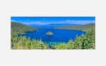 Panoramic view of the blue waters of Lake Tahoe with surrounding green forests and mountain ranges under a clear sky.