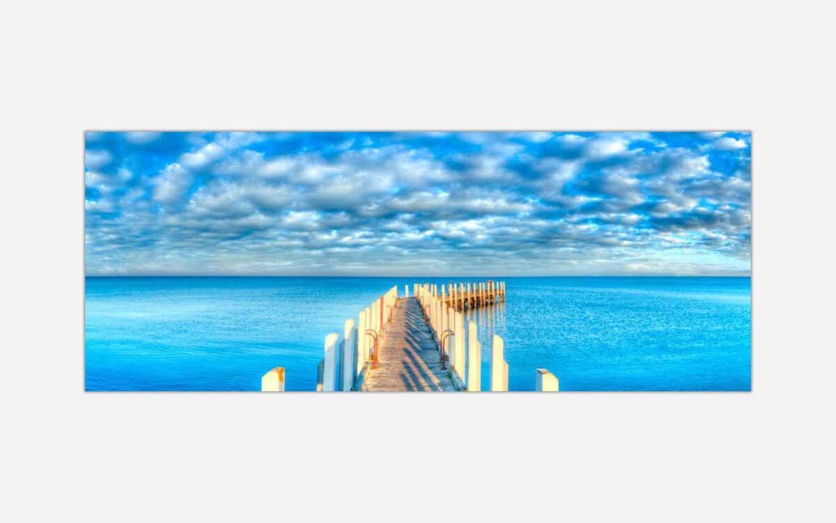 A panoramic canvas print of a wooden pier extending into a calm blue ocean with a cloudy sky above.