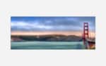 A panoramic photograph of the Golden Gate Bridge at sunset with colorful skies and calm sea in the foreground.