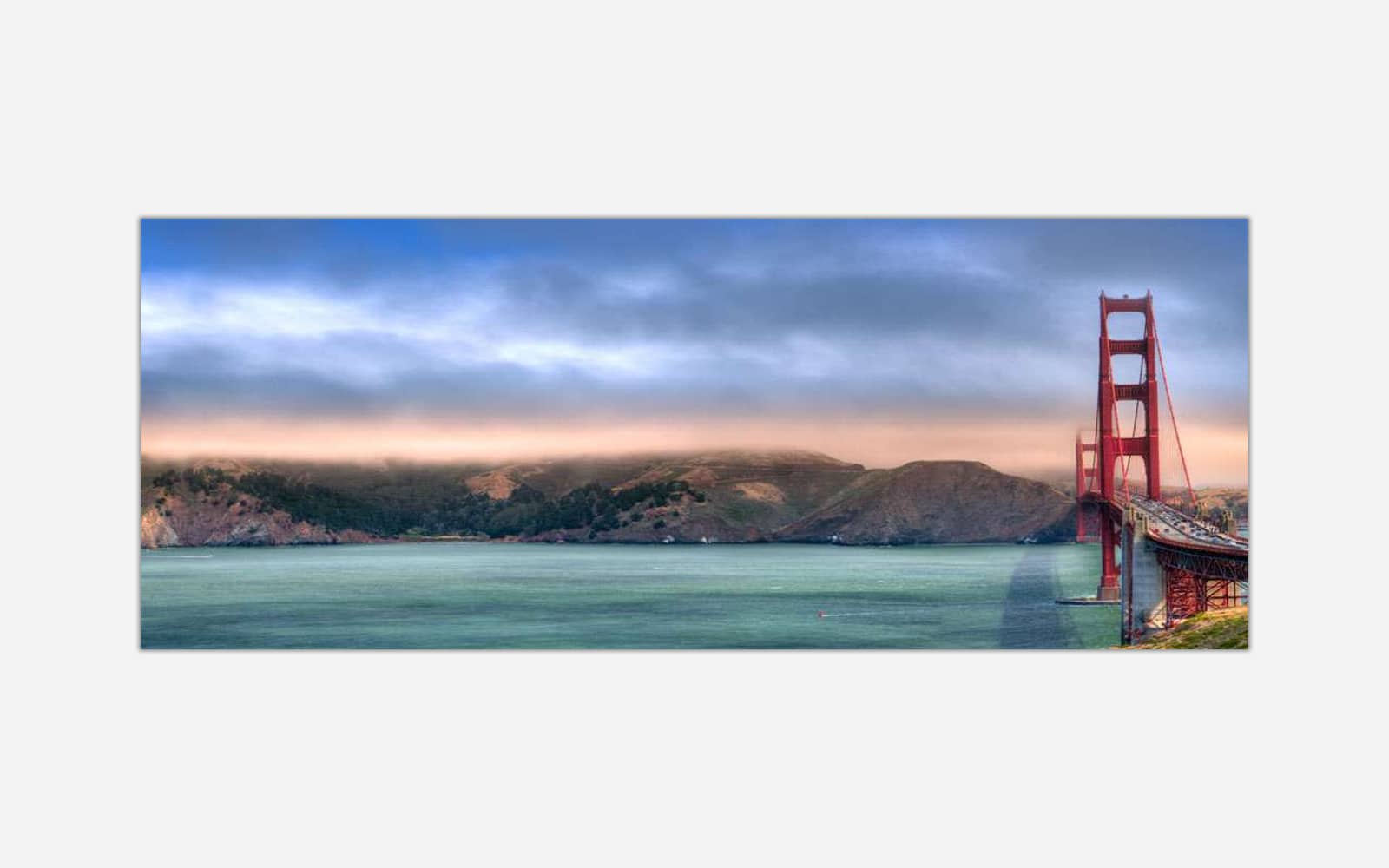 Golden Gate Panoramic (1) A panoramic photograph of the Golden Gate Bridge at sunset with colorful skies and calm sea in the foreground.
