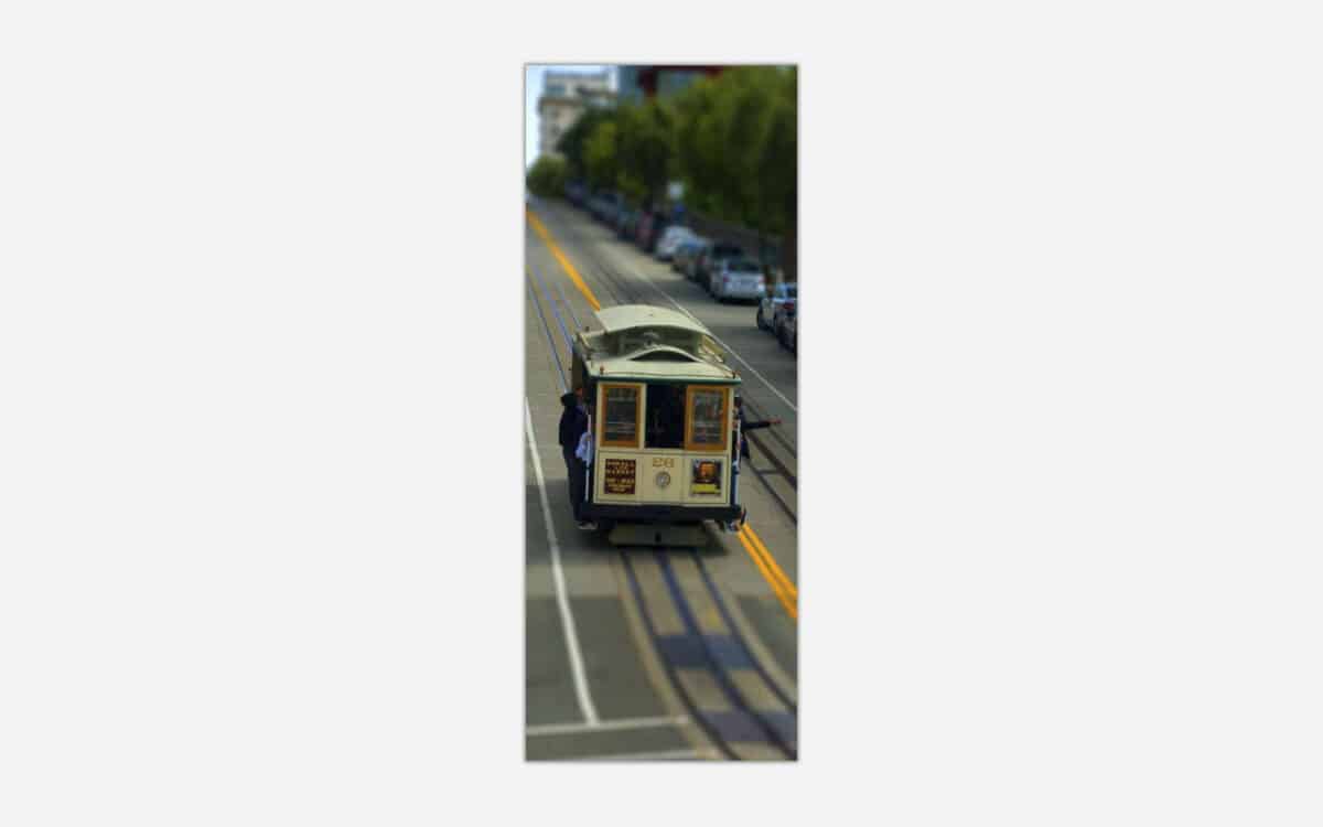 A tilt-shift photograph of a classic San Francisco cable car on the streets with blurred surrounding details giving a miniature effect.