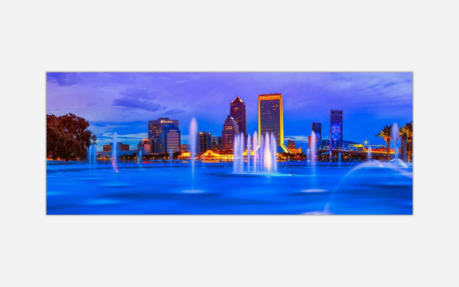 Jacksonville II (1) Long exposure photograph of a city skyline at dusk with illuminated buildings and fountain lights, with smooth water foreground due to long exposure technique.