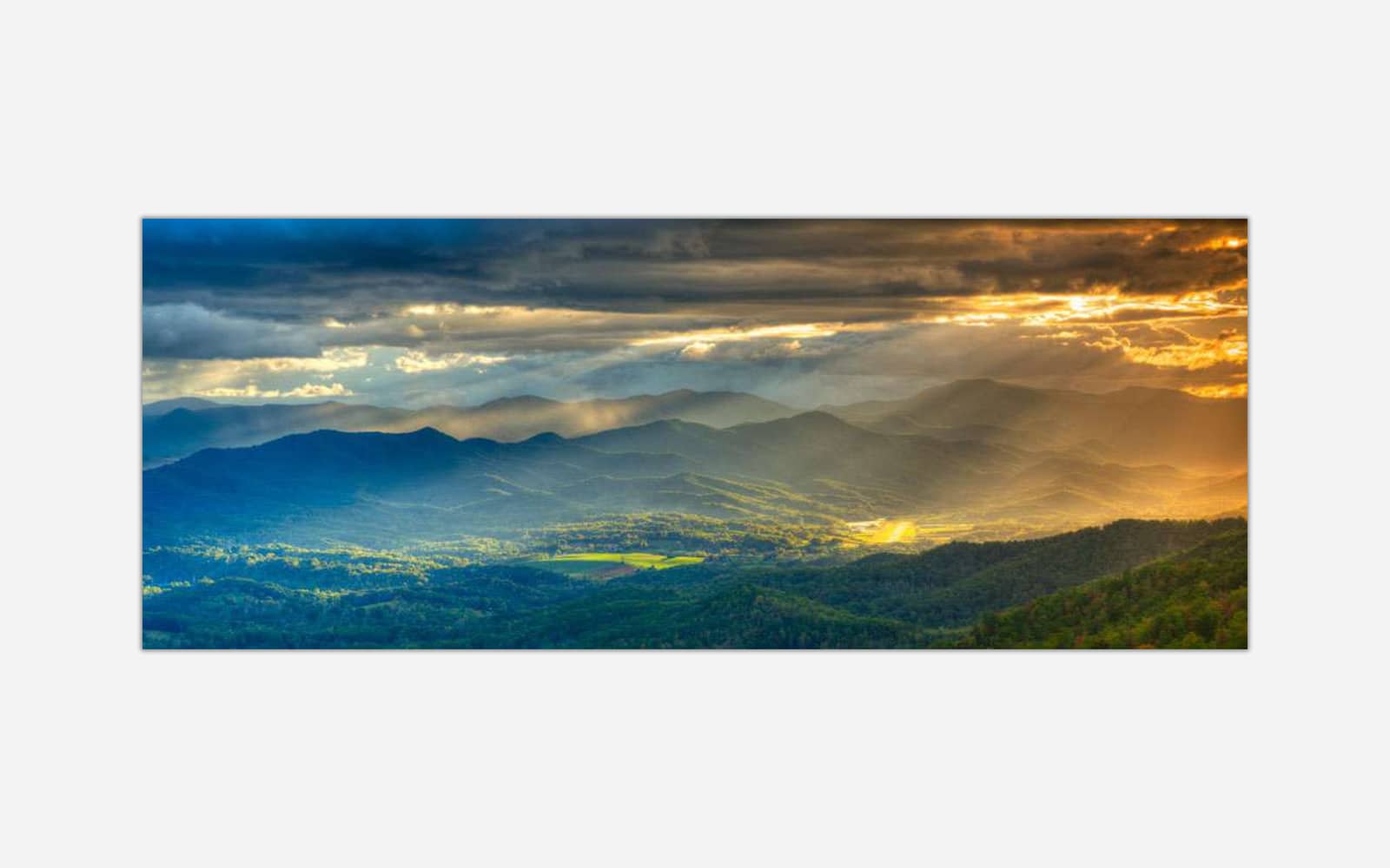 Lost in the Valley of Dreams (1) A panoramic landscape photograph of a mountain range during sunset with sunbeams breaking through clouds, casting a golden light over the valleys.