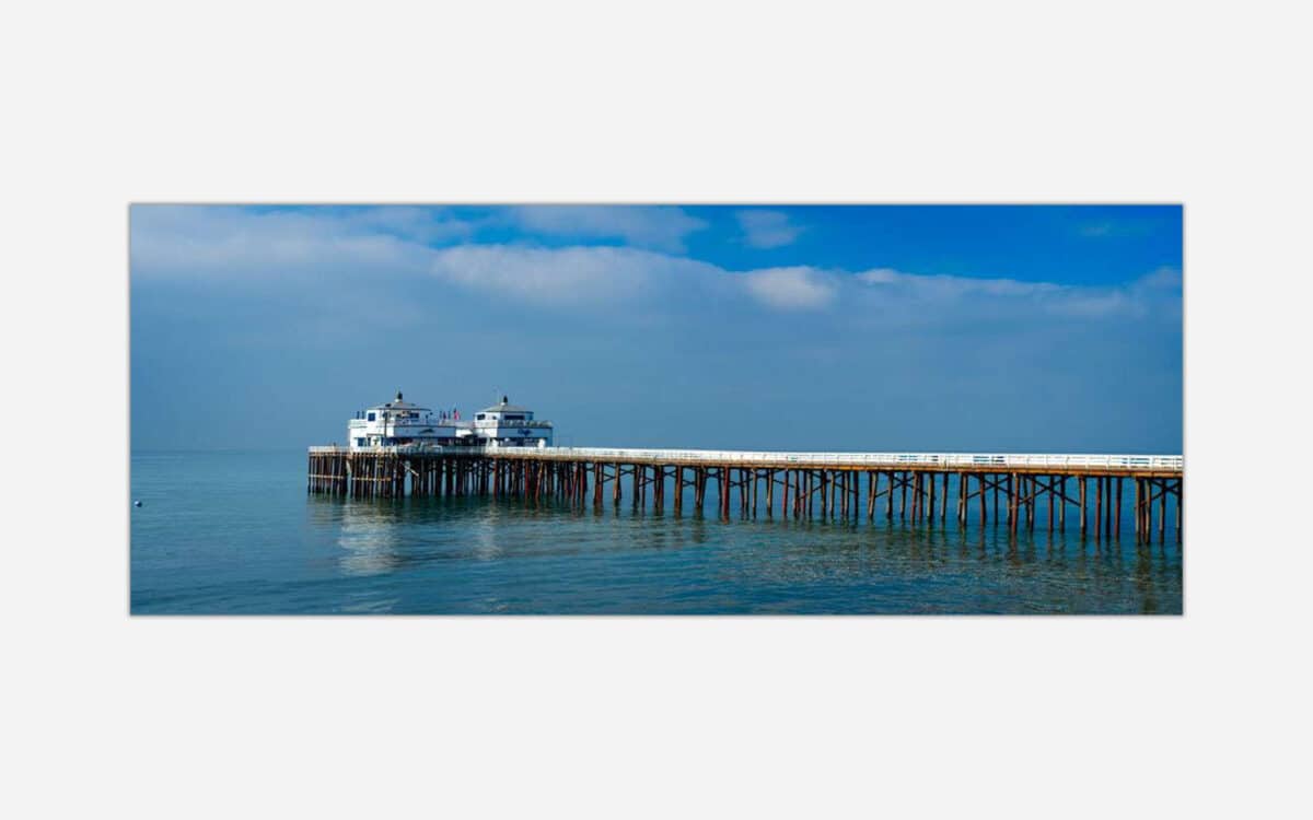 A photograph of a long wooden pier extending into the calm blue ocean under a clear sky.