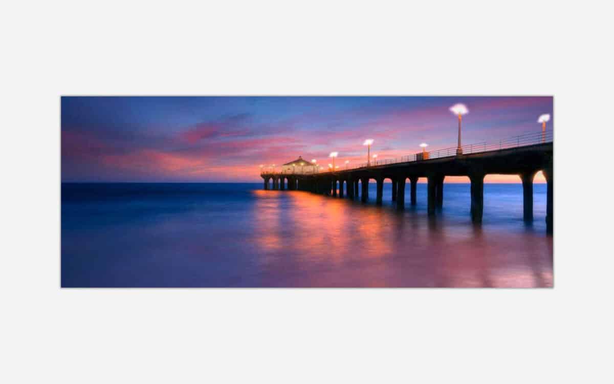 An image of a pier extending into the ocean with a vibrant sunset in the background and light reflections on water.