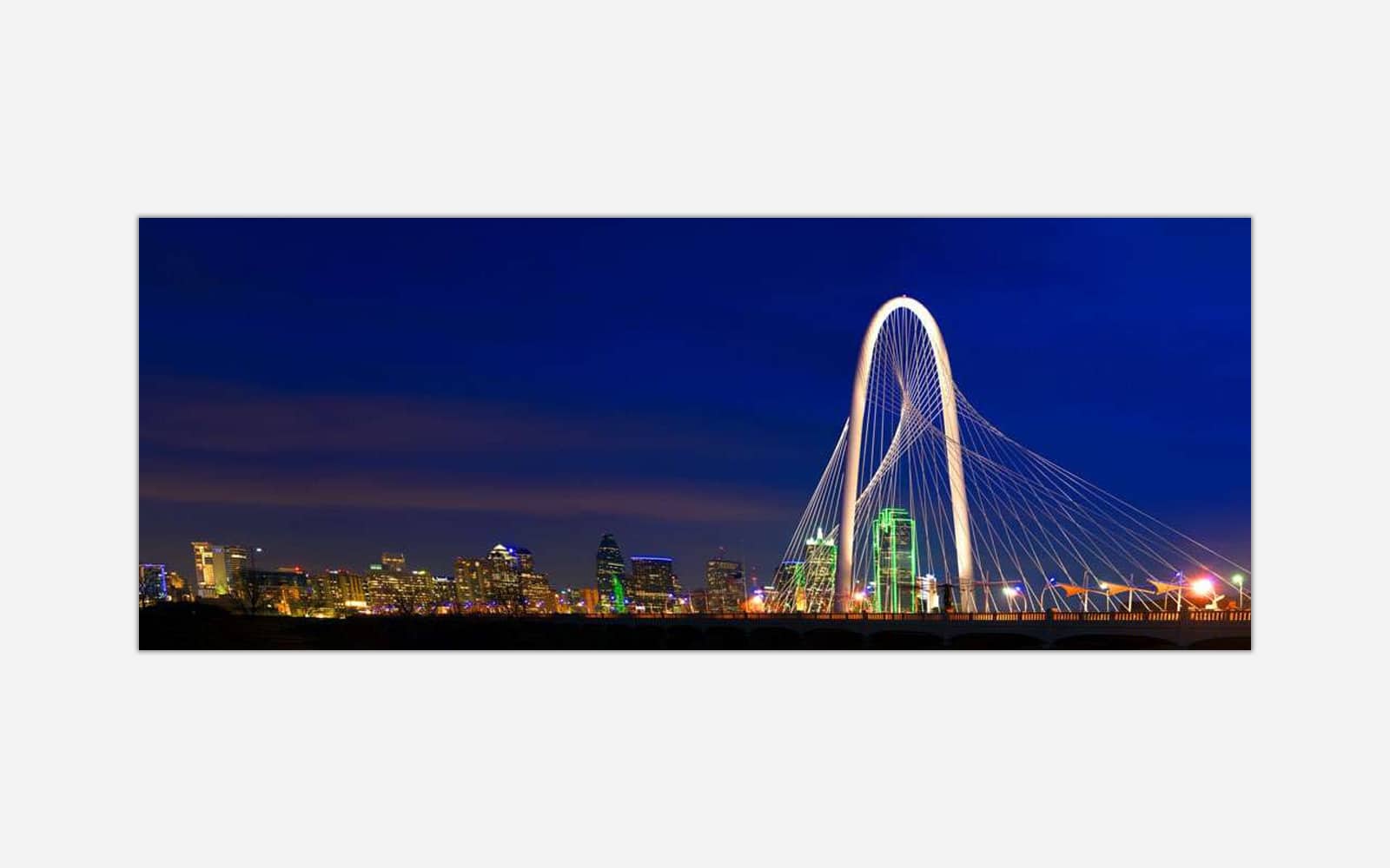 Margaret Hunt Hill bridge (1) A panoramic view of the illuminated Dallas skyline at night with the prominent Margaret Hunt Hill Bridge in the foreground.