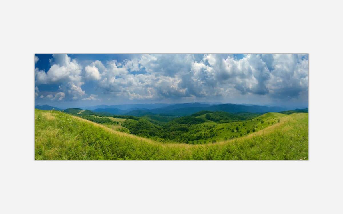 Panoramic landscape photograph of rolling green hills under a cloudy blue sky.