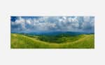 Panoramic landscape photograph of rolling green hills under a cloudy blue sky.