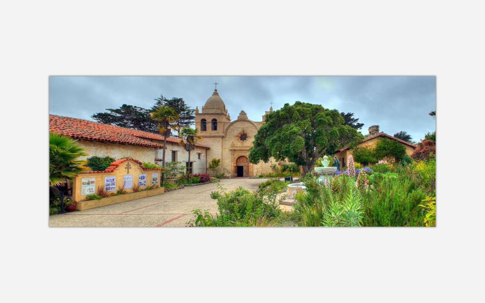 Mission San Carlos (1) A high dynamic range (HDR) image of a historic California mission with Spanish colonial architecture surrounded by a lush garden and a fountain in the courtyard.