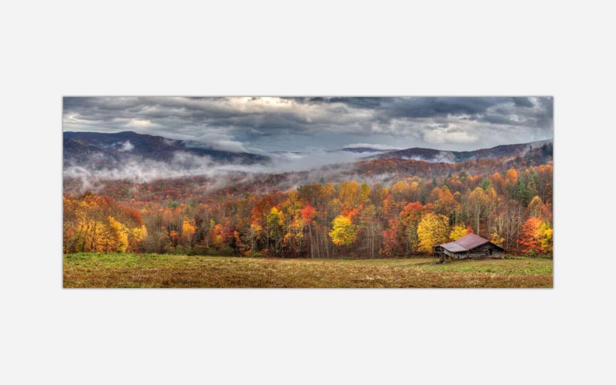 A panoramic photograph of a rustic cabin amidst a colorful autumn forest with misty mountains in the background.