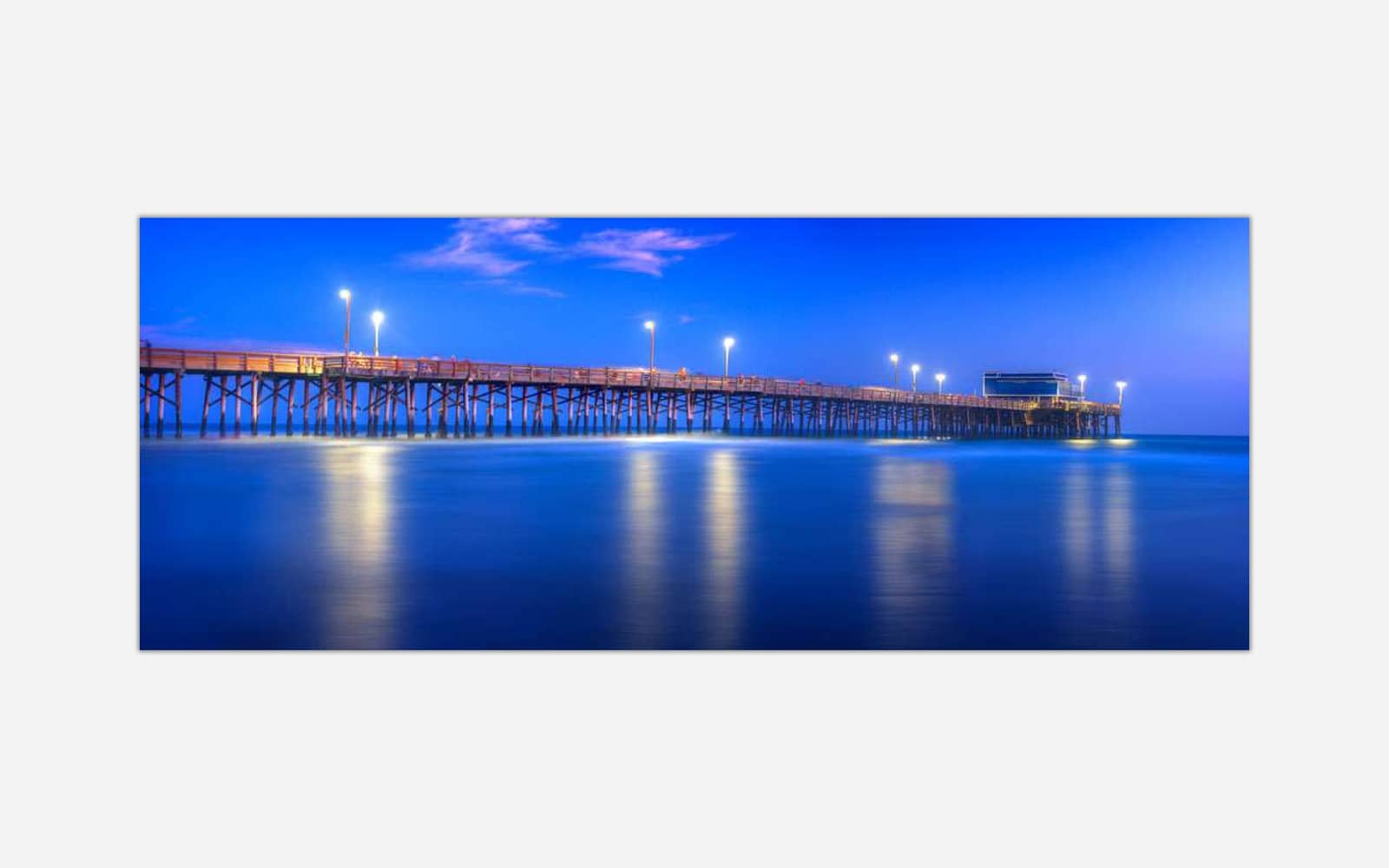 Newport Pier (1) A long exposure photograph of a wooden pier extending into serene blue waters under a twilight sky illuminated by lamp lights.