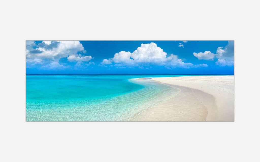 A panoramic canvas print of a tranquil tropical beach with vivid turquoise sea, white sand, and a clear blue sky with fluffy clouds.