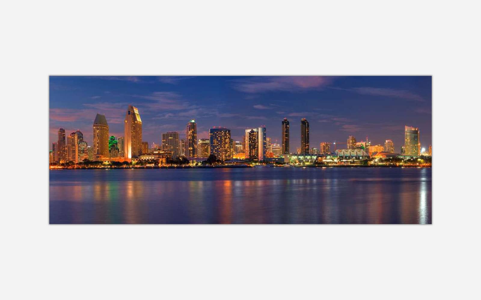 San Diego (1) A panoramic view of a city skyline at twilight with illuminated buildings reflecting on the water.