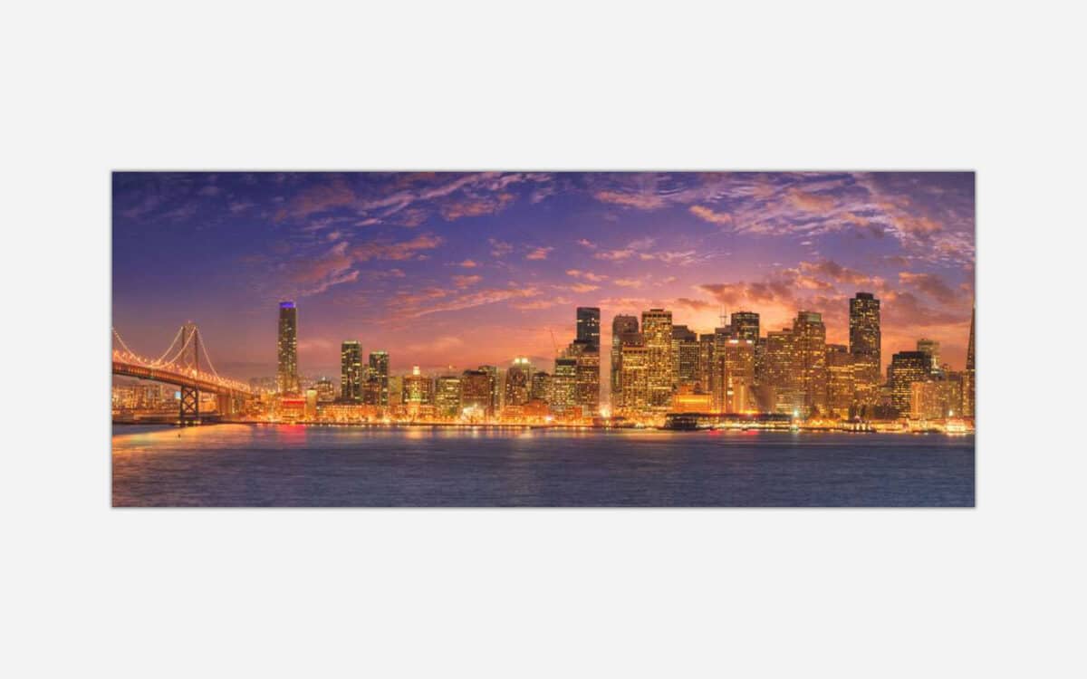 A panoramic cityscape art piece depicting a vibrant sunset over a city with skyscrapers, lit buildings, and a bridge over water.