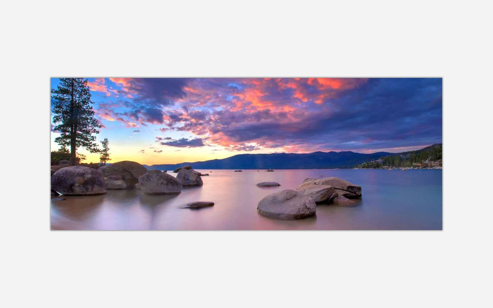 Sand Harbor Beach (1) A panoramic photo of a serene lake with colorful sunset skies, silhouetted mountains in the background, and smooth water with rocks in the foreground.