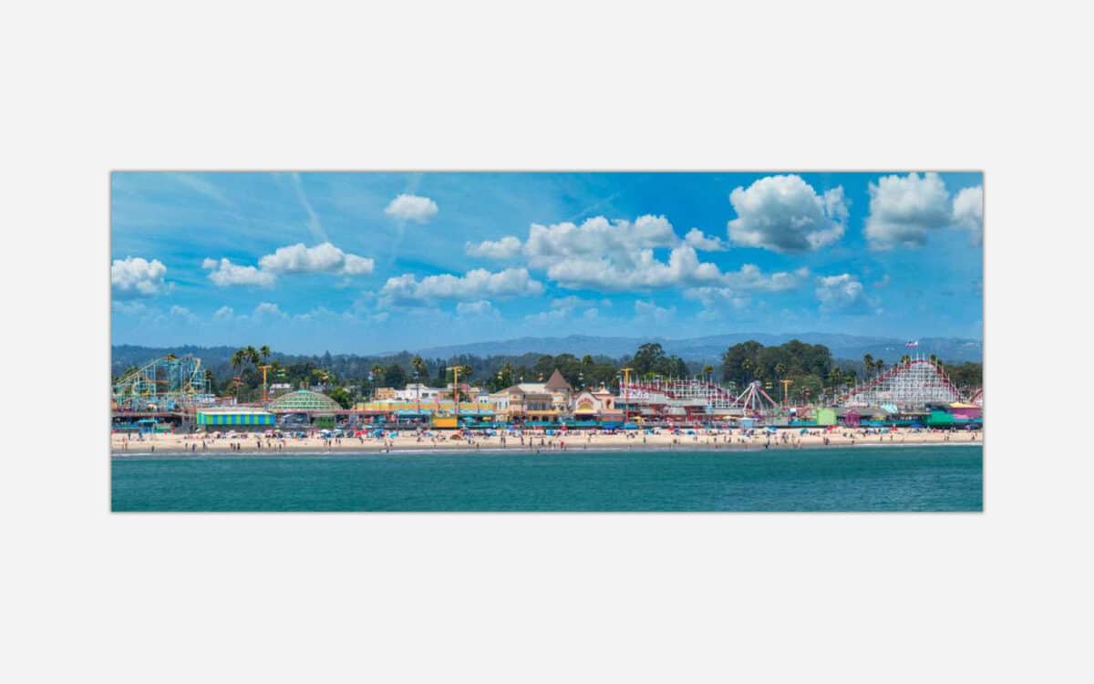 A vibrant art print featuring a seaside amusement park with a roller coaster, colorful buildings, beachgoers, and a clear blue sky.