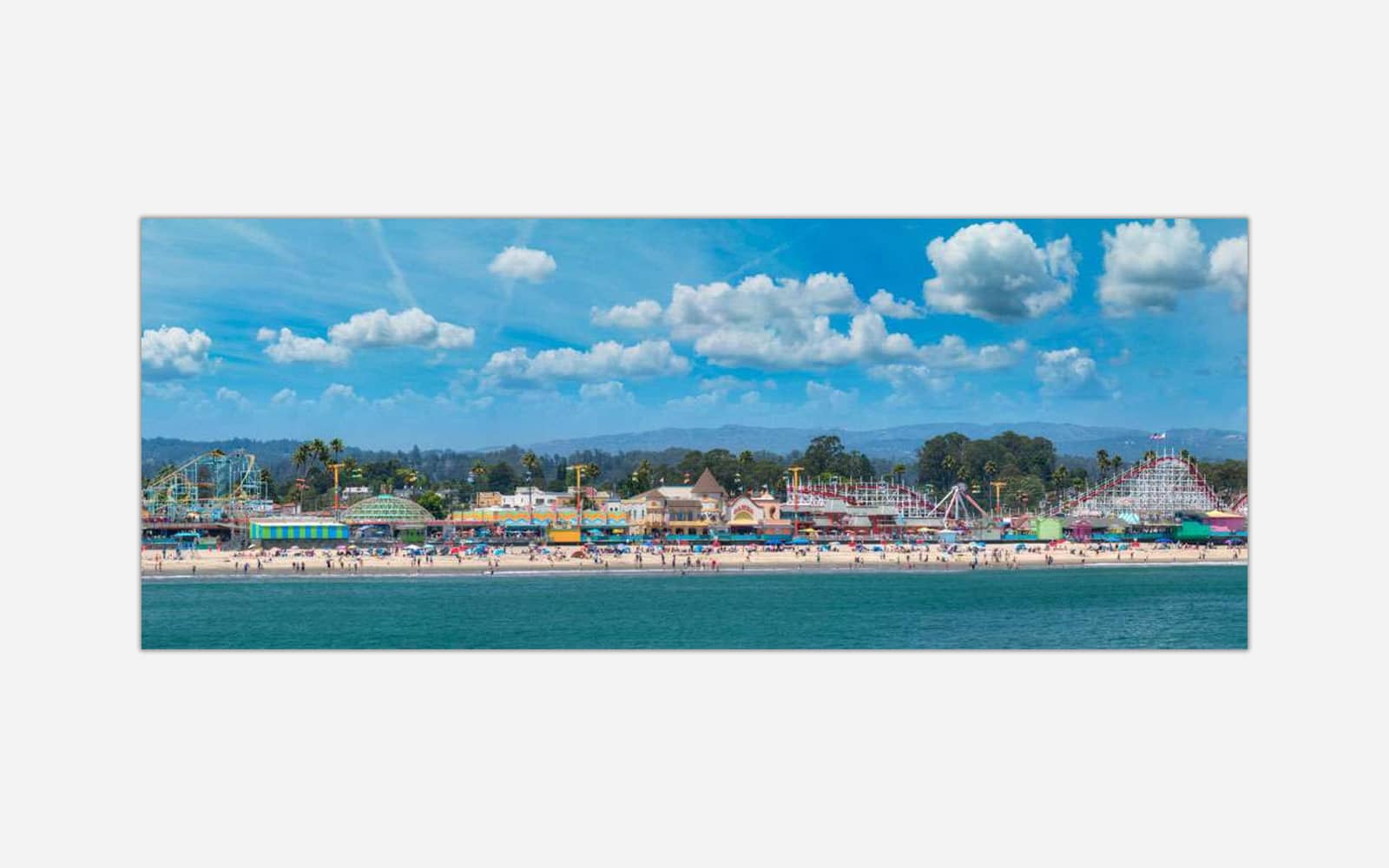 Santa Cruz Boardwalk (1) A vibrant art print featuring a seaside amusement park with a roller coaster, colorful buildings, beachgoers, and a clear blue sky.