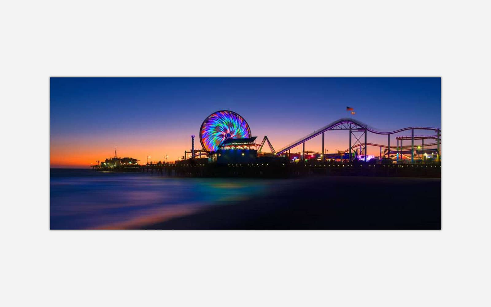 Santa Monica Pier (1) A photograph of a beach pier amusement park at sunset with a colorful Ferris wheel and roller coaster silhouettes against a twilight sky.