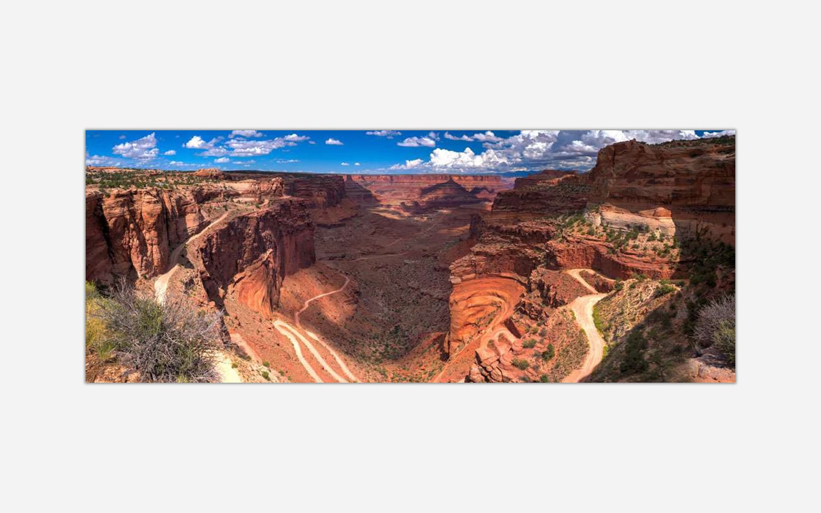 Shafer Trail (1) Panoramic photo of a meandering canyon with red rock formations under a blue sky with clouds.