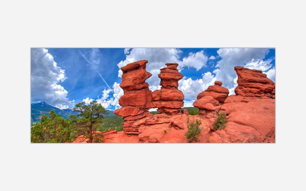 A high dynamic range photograph of distinctive red rock formations with a lush green landscape and a dramatic blue sky with clouds in the background.