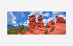A high dynamic range photograph of distinctive red rock formations with a lush green landscape and a dramatic blue sky with clouds in the background.
