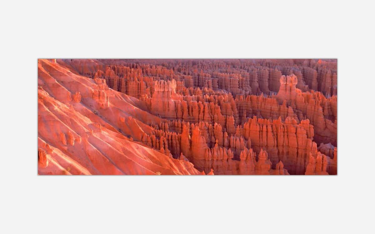 A panoramic photograph of the reddish-orange hoodoos and rock formations of Bryce Canyon National Park at sunset.