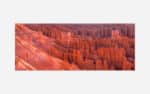 A panoramic photograph of the reddish-orange hoodoos and rock formations of Bryce Canyon National Park at sunset.