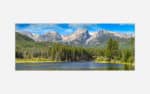 A panoramic photograph of a mountain landscape with a forest and lake in the foreground and a blue sky above.
