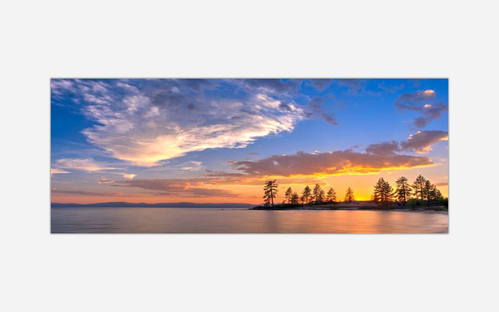 Tahoe Sunset (2) A panoramic photograph of a sunset with golden and orange hues in the sky, silhouetted trees against a calm lake with dramatic clouds above.