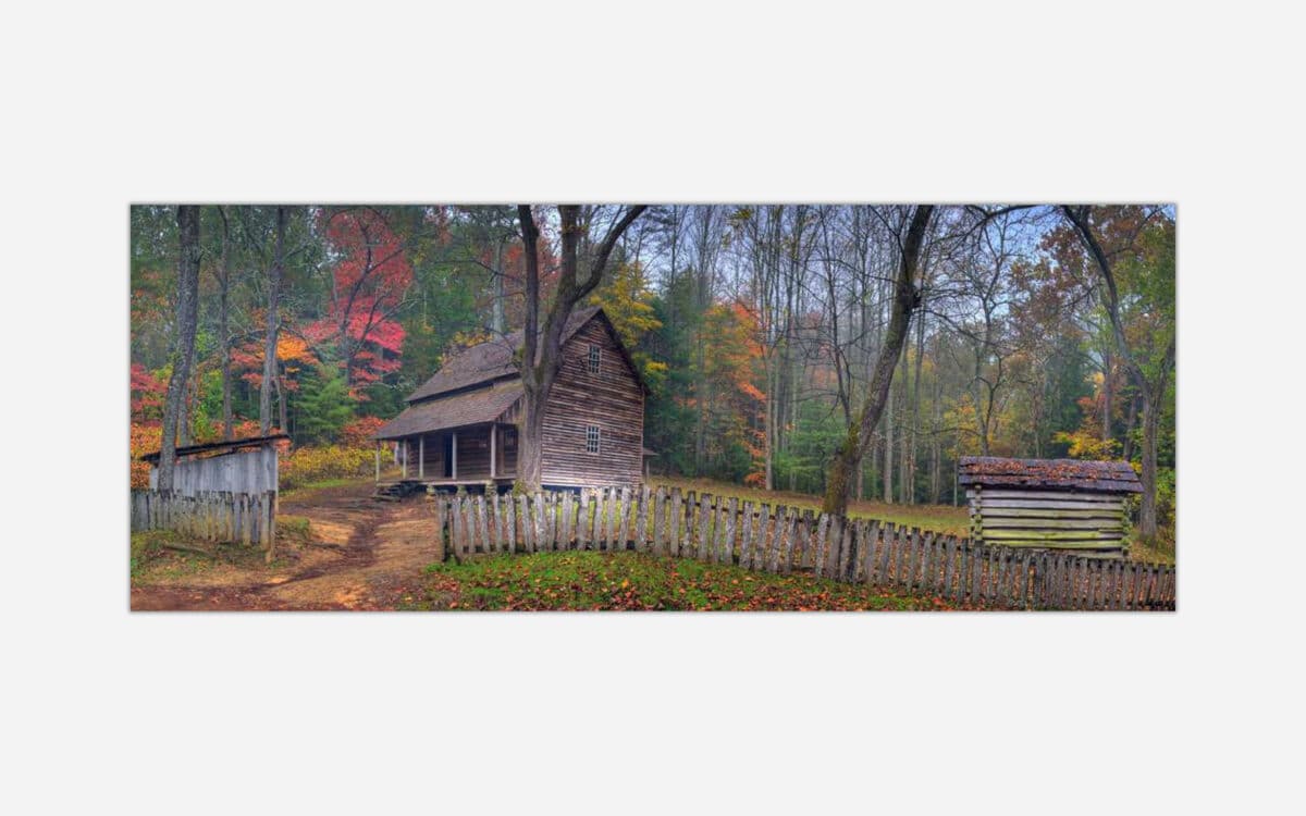 An image of an old wooden cabin surrounded by a rustic fence amidst trees with autumn foliage.