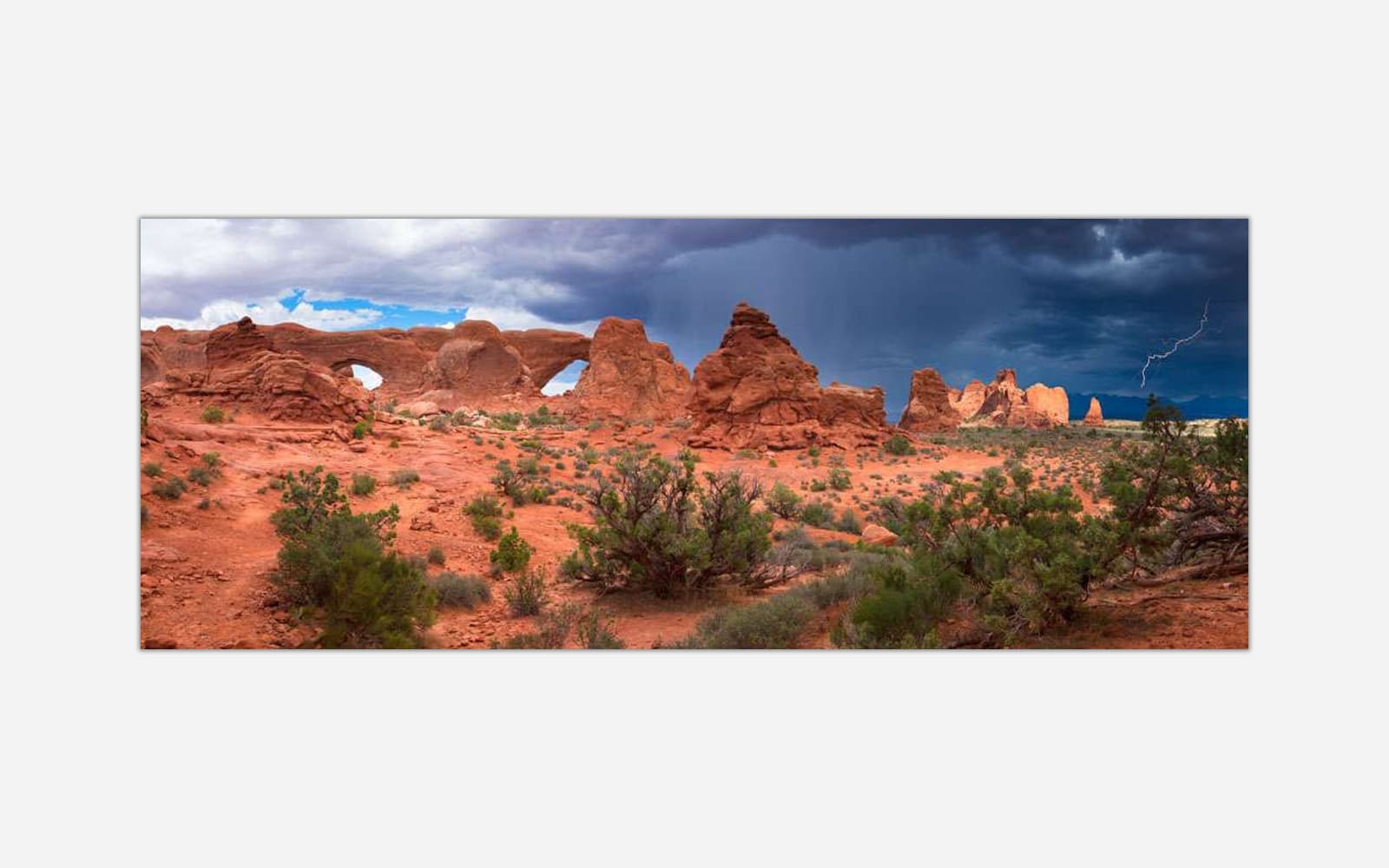 The Windows (1) A panoramic photograph of Arches National Park with dramatic storm clouds and a lightning bolt in the distance over red desert rock formations.
